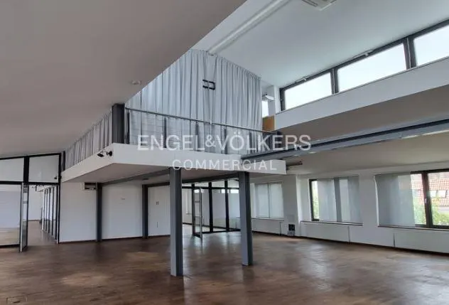 Interior view of a commercial space with a mezzanine, large windows, and wooden floors. The Engel & Volkers Commercial logo is visible.