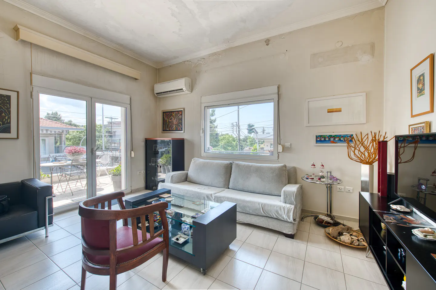 Living room with a light gray sofa, glass coffee table, wooden armchair, and glass balcony doors leading to a terrace.