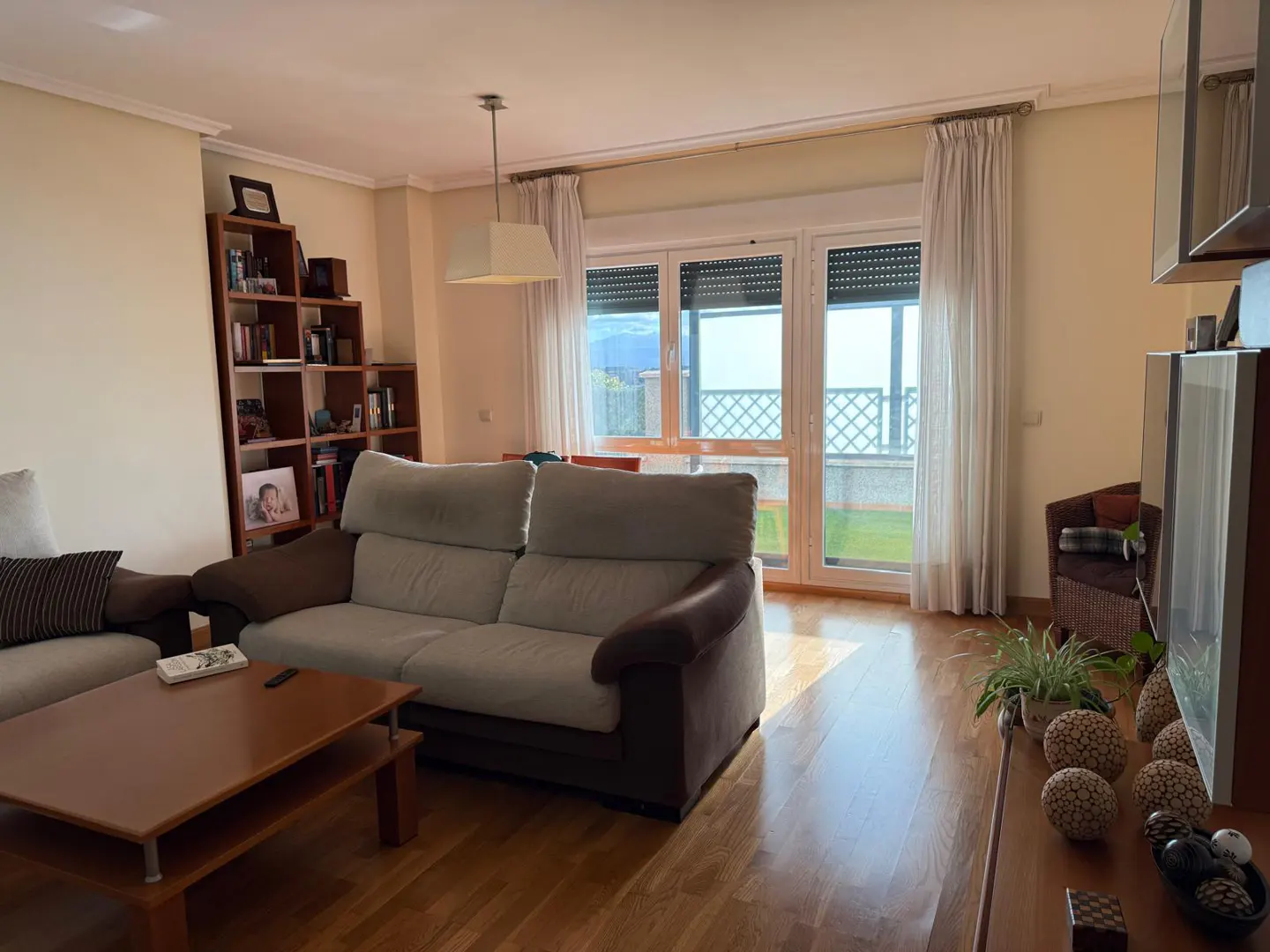 Living room with a gray sofa, brown coffee table, and a bookshelf. Large windows offer a view of the outside.