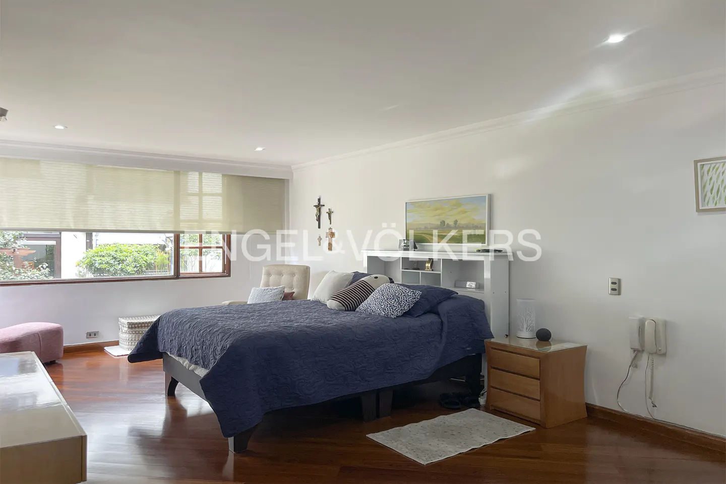 Bedroom with a blue quilt on the bed, a wooden floor, and a window with blinds.