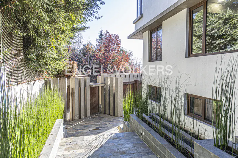 Exterior of a modern white house with brown window frames, stone walkway, and green plants.