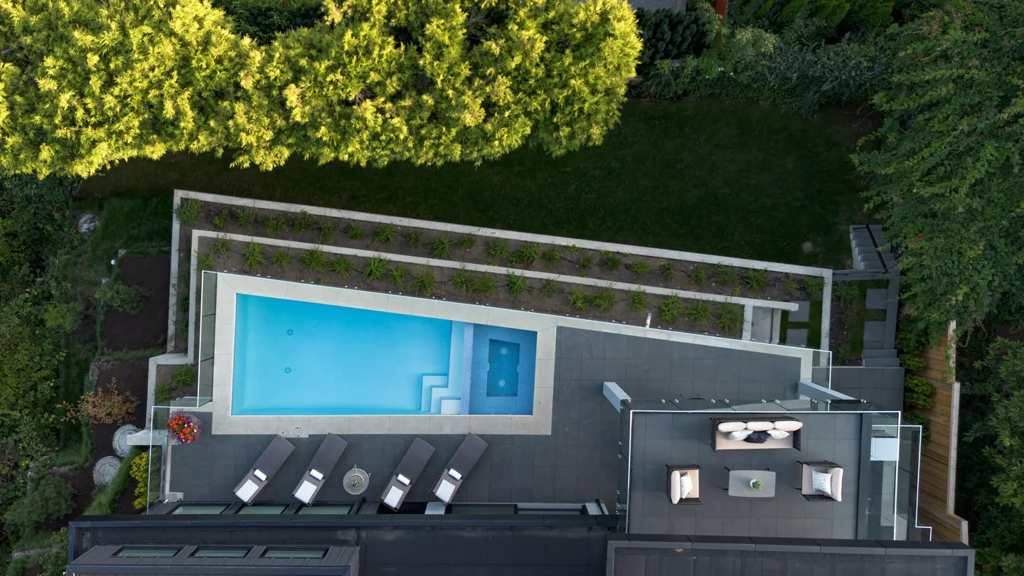 Aerial view of a modern home with a pool, lounge chairs, and outdoor seating area surrounded by lush greenery.