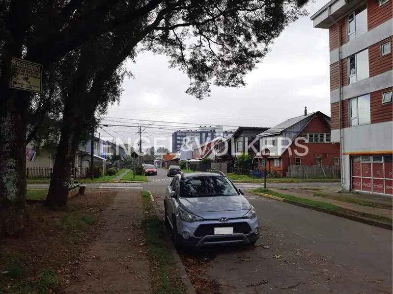 Street view with a parked gray car, crosswalk, and houses. The sky is overcast. Engel & Volkers logo is visible.