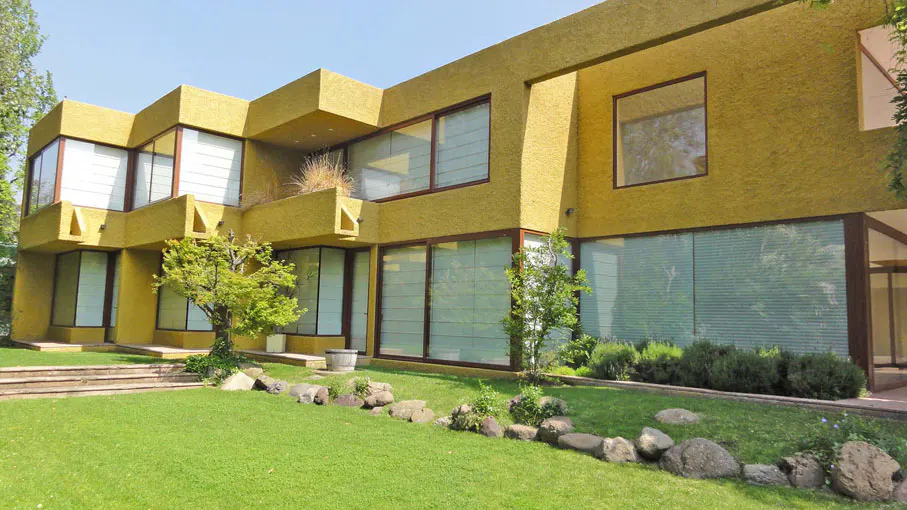 A modern, yellow house with large windows and a green lawn. A rock border separates the lawn from the house.