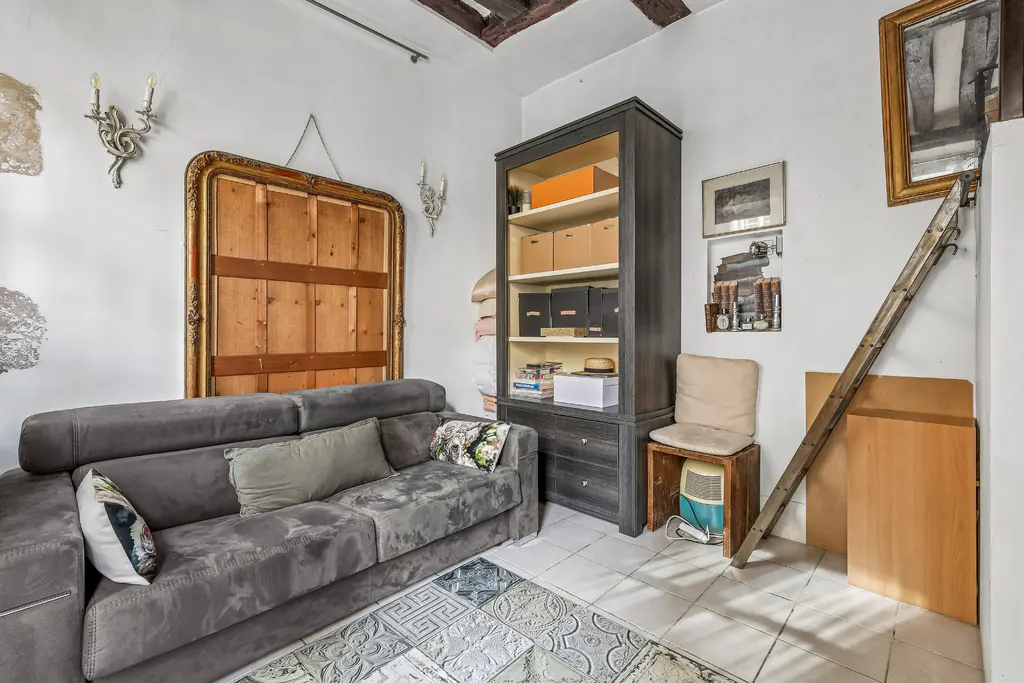 Living room with gray sofa, wooden bookcase, and ladder leaning against the wall. The walls are white and there is a patterned rug on the floor.
