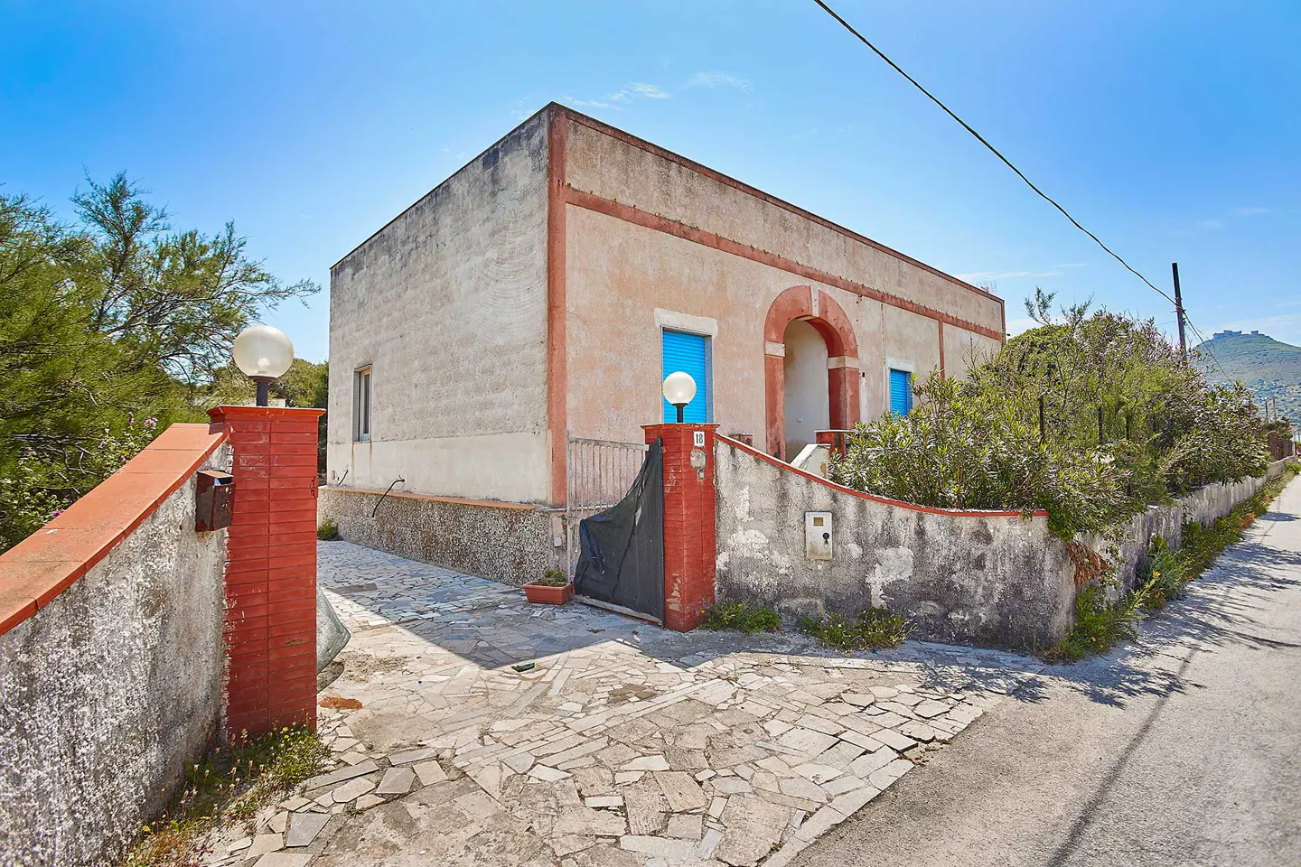 Single-story peach-colored house with blue shutters, stone driveway, and red brick accents under a clear blue sky.