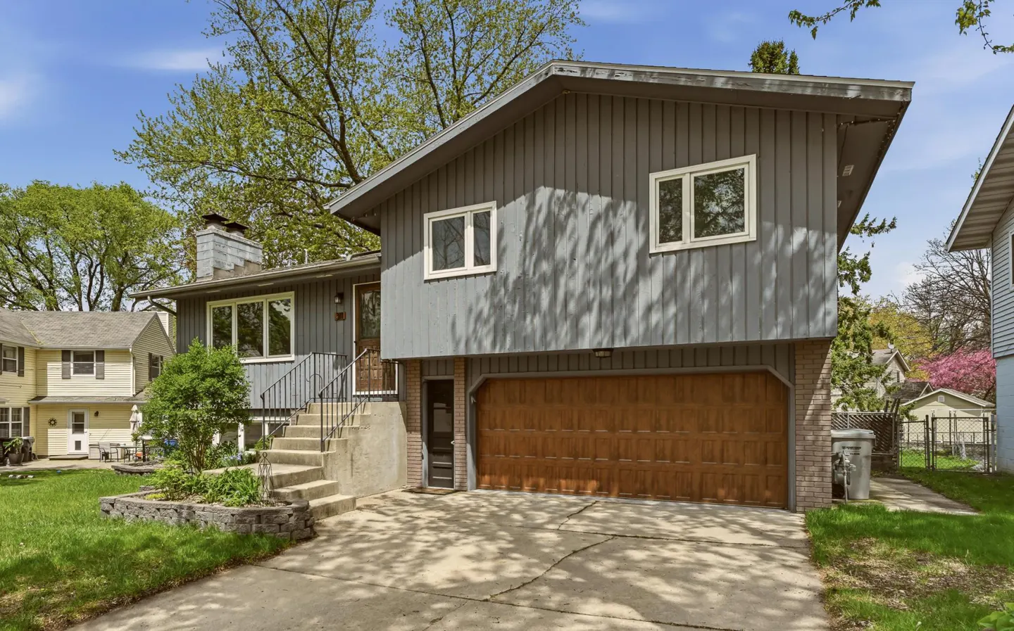 Exterior of a two-story gray house with a brown garage door and concrete steps leading to the front door.
