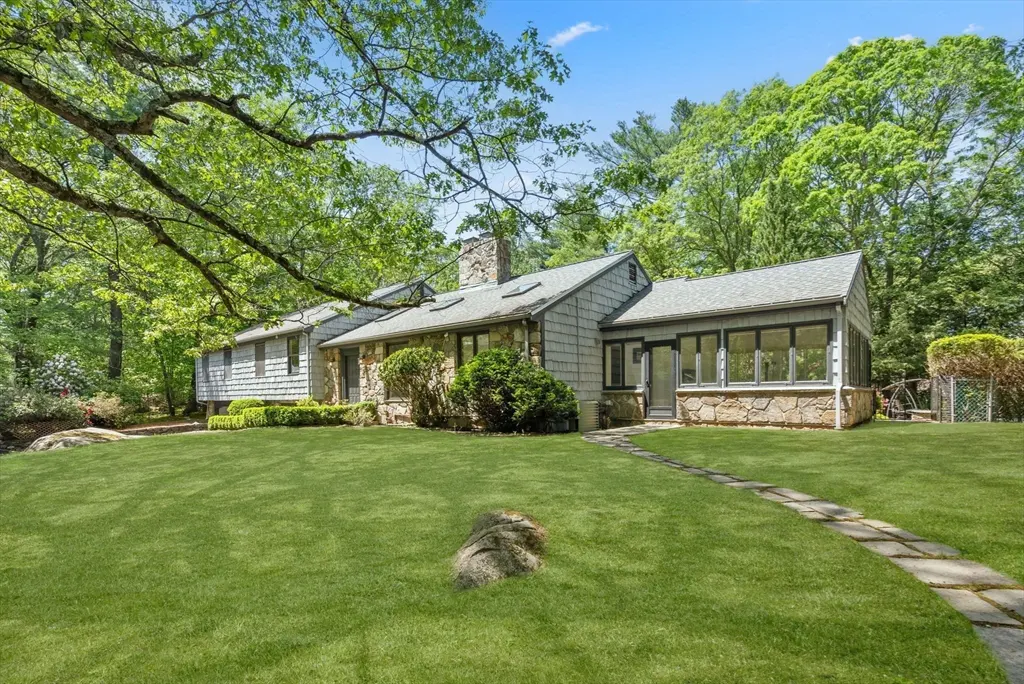 Exterior view of a gray stone and shingle house with a stone chimney and a green lawn.