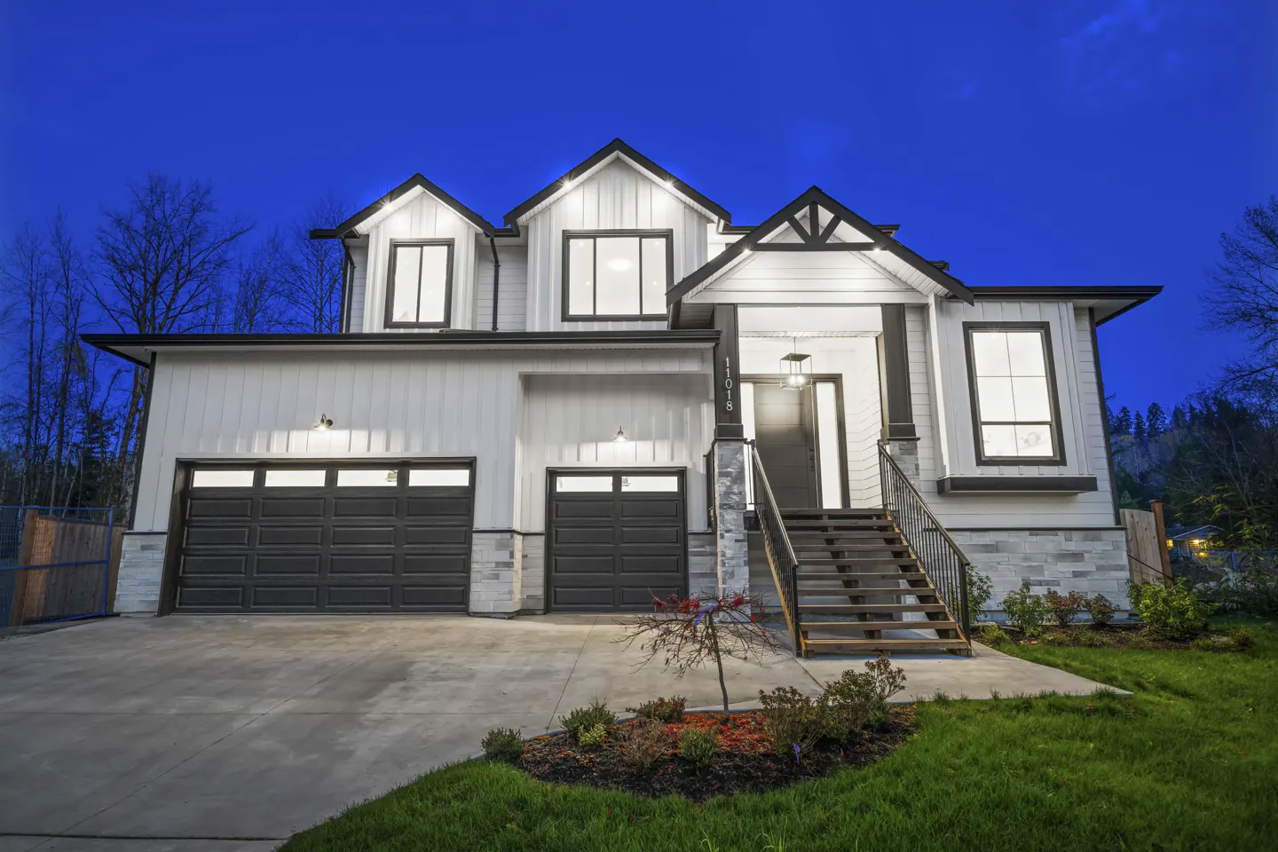 Two-story house with white siding, black trim, and a two-car garage at dusk. Stairs lead to the front door.
