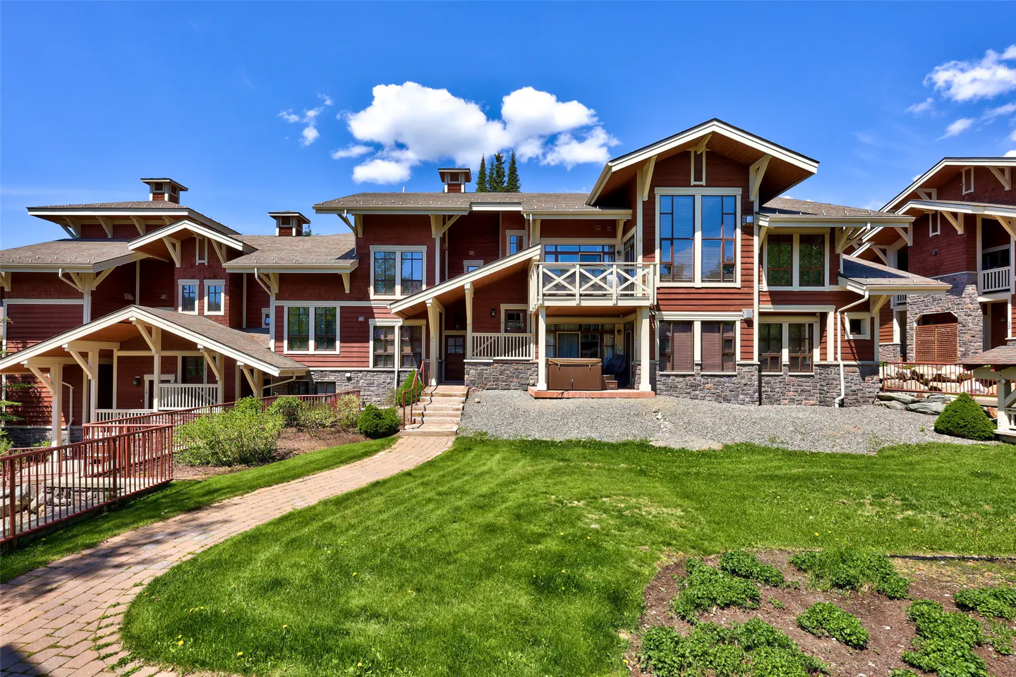 Exterior of a red, multi-story home with stone accents, a brick walkway, and a green lawn under a blue sky.