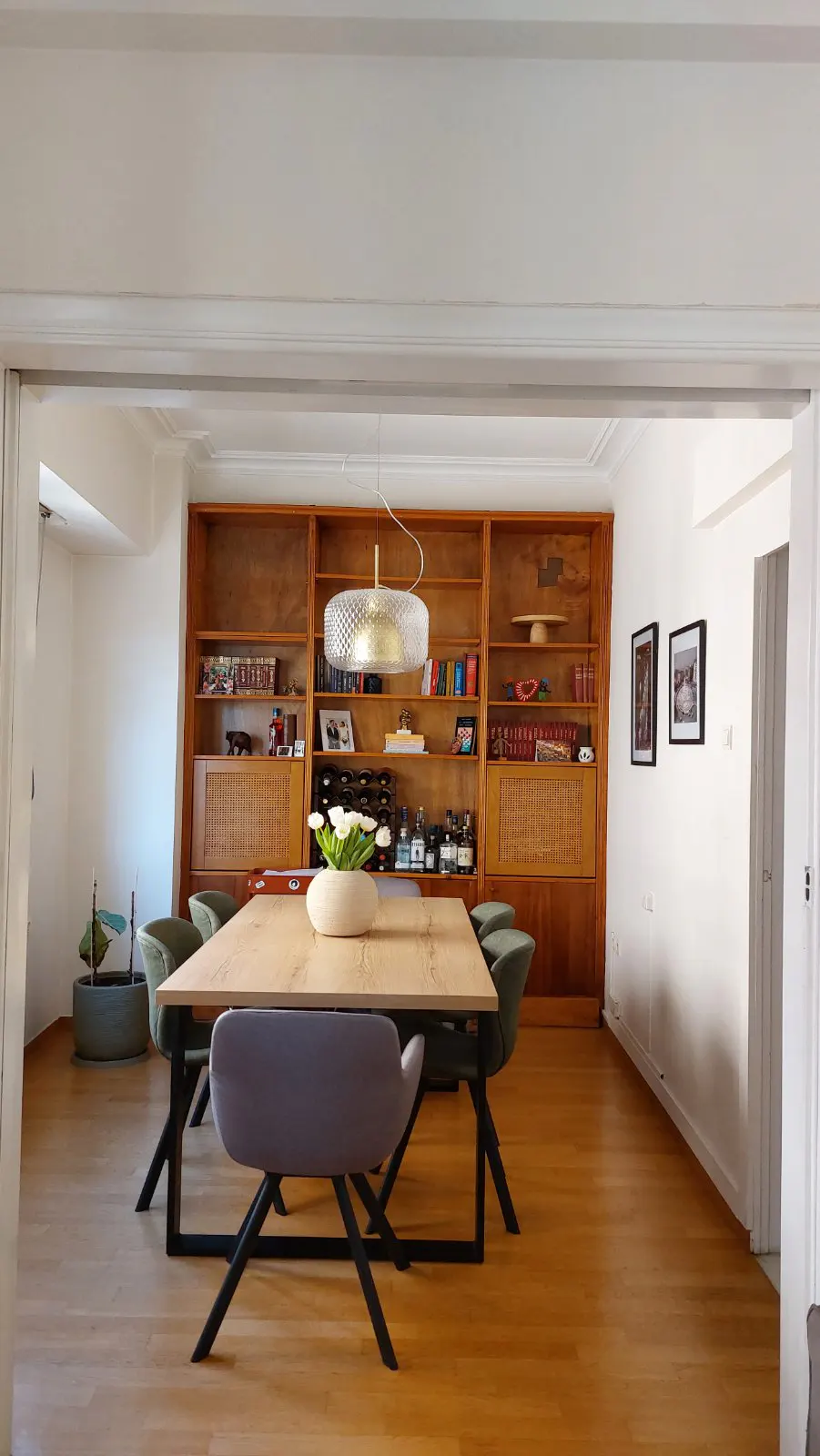 A dining room with a wooden table, gray and green chairs, and a large wooden bookshelf in the background.