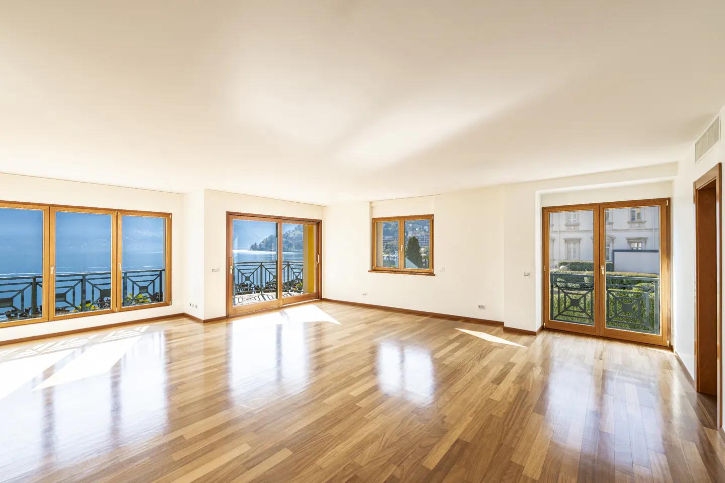Bright, empty room with hardwood floors, white walls, and large windows with lake views.