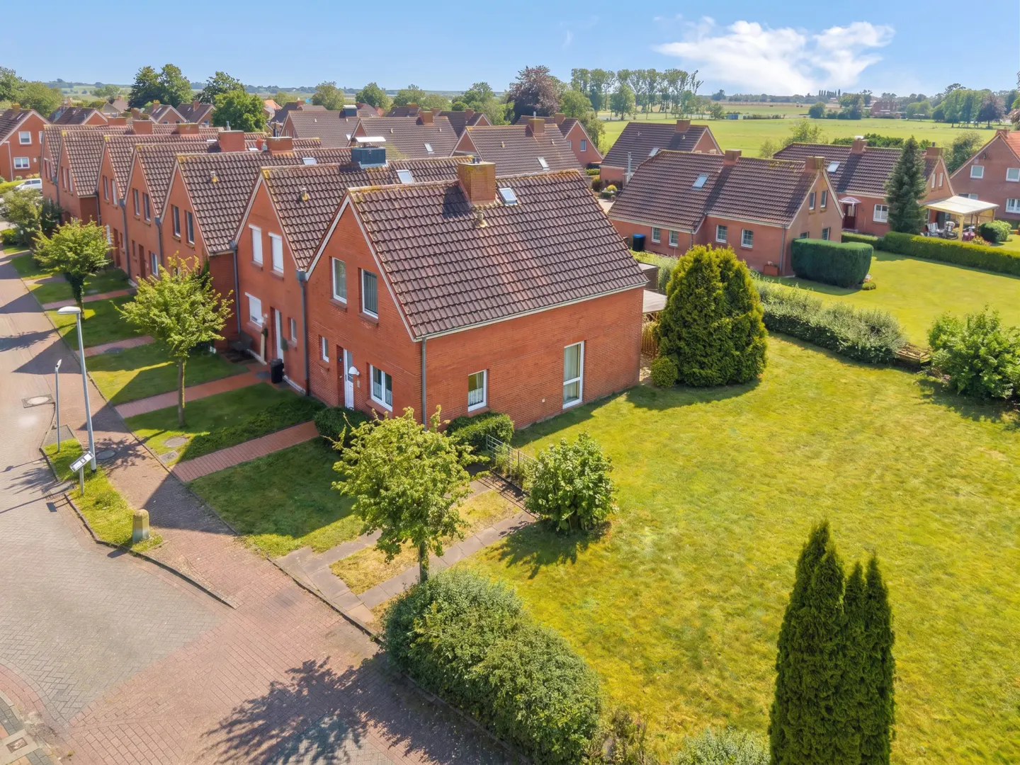 Aerial view of a row of red brick houses with brown roofs, green lawns, and a blue sky.