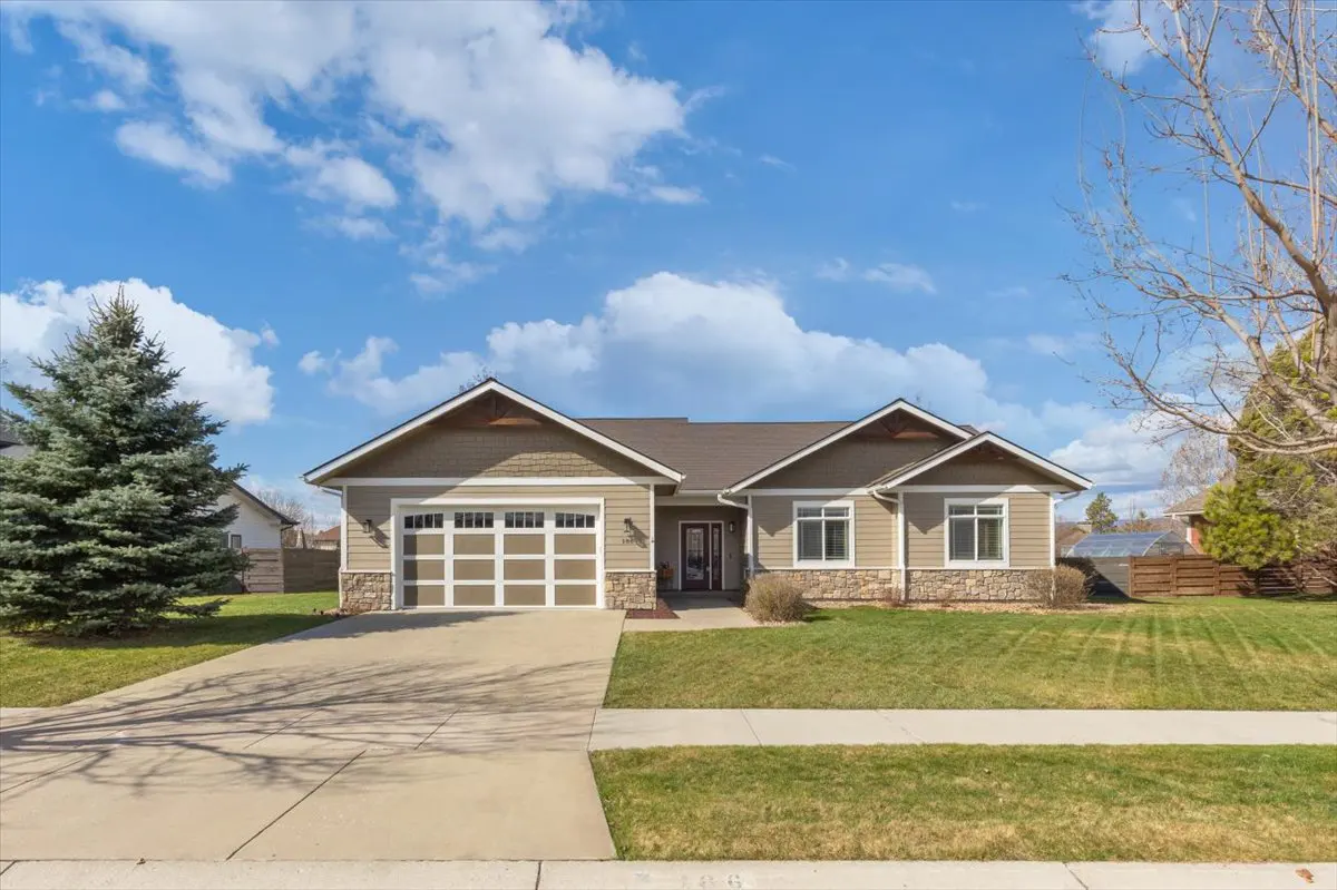 Front exterior of a one-story, beige house with a brown roof, white garage door, and green lawn.