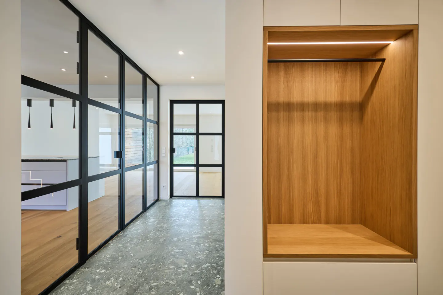 Modern interior with black-framed glass doors, a gray terrazzo floor, and a built-in wooden closet with a shelf and hanging rod.