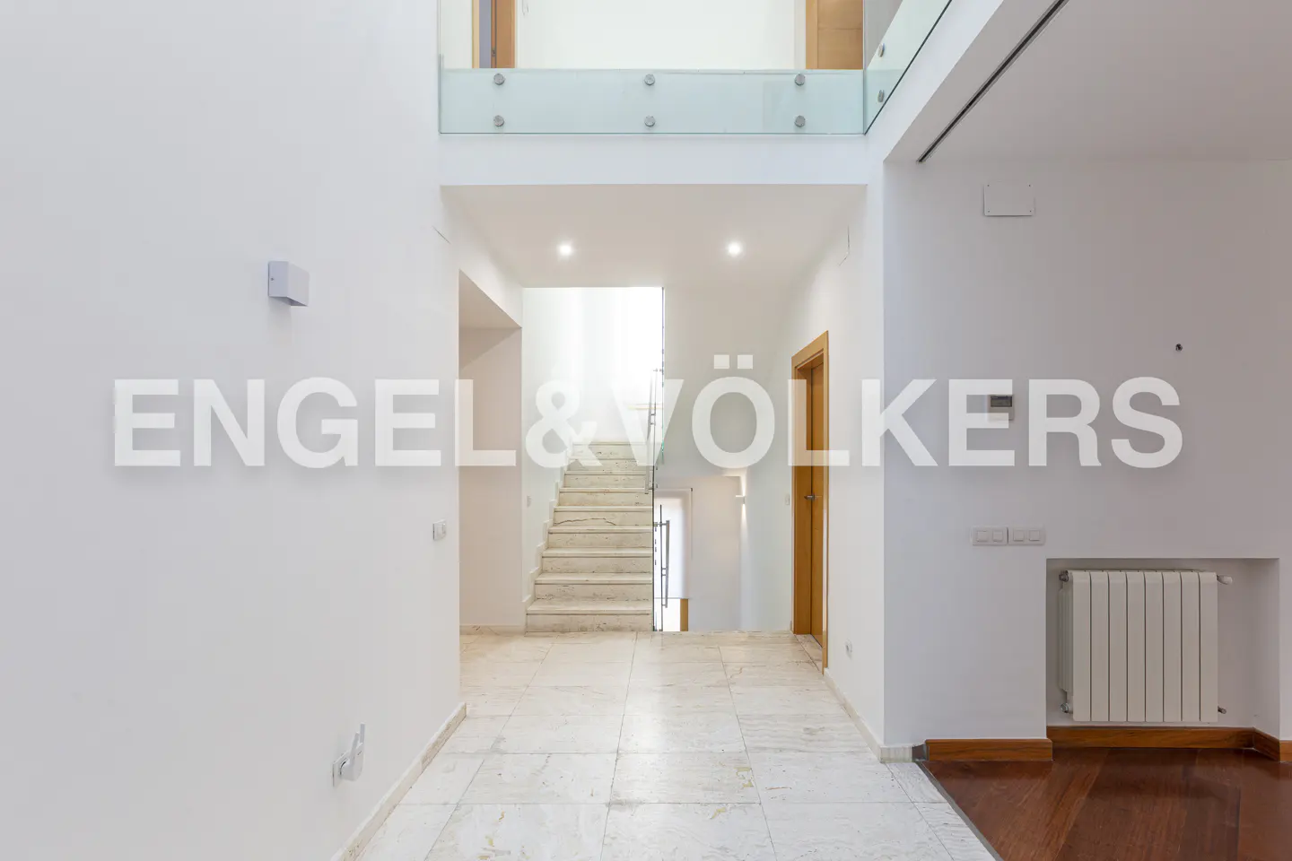 Bright, modern foyer with marble floors, white walls, and a staircase leading up. Engel & Völkers logo visible.