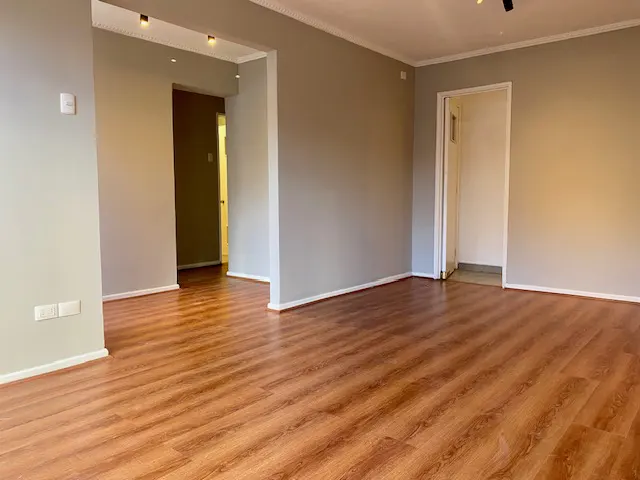 Empty room with wood-look floors, gray walls, and white trim. Doorways lead to other rooms. Spotlights on the ceiling.