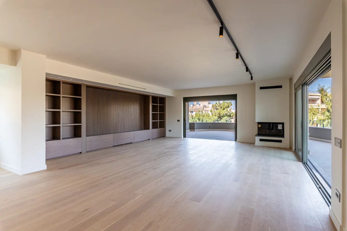 Modern living room with light wood floors, a large built-in wooden shelving unit, a fireplace, and a balcony view.