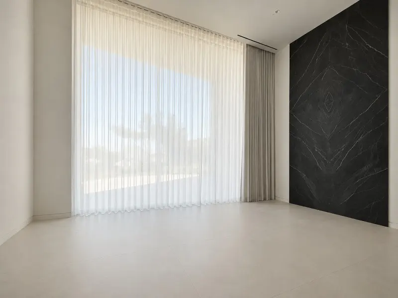 An empty room with white walls, sheer curtains over a large window, and a black marble accent wall.