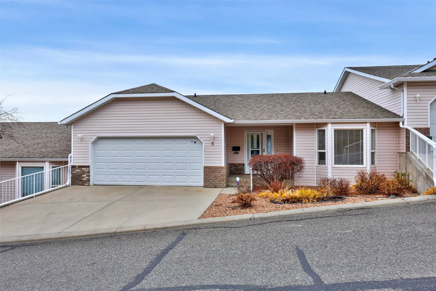 Beige single-story house with a white garage door, brown roof, and a small garden in front. Blue sky above.