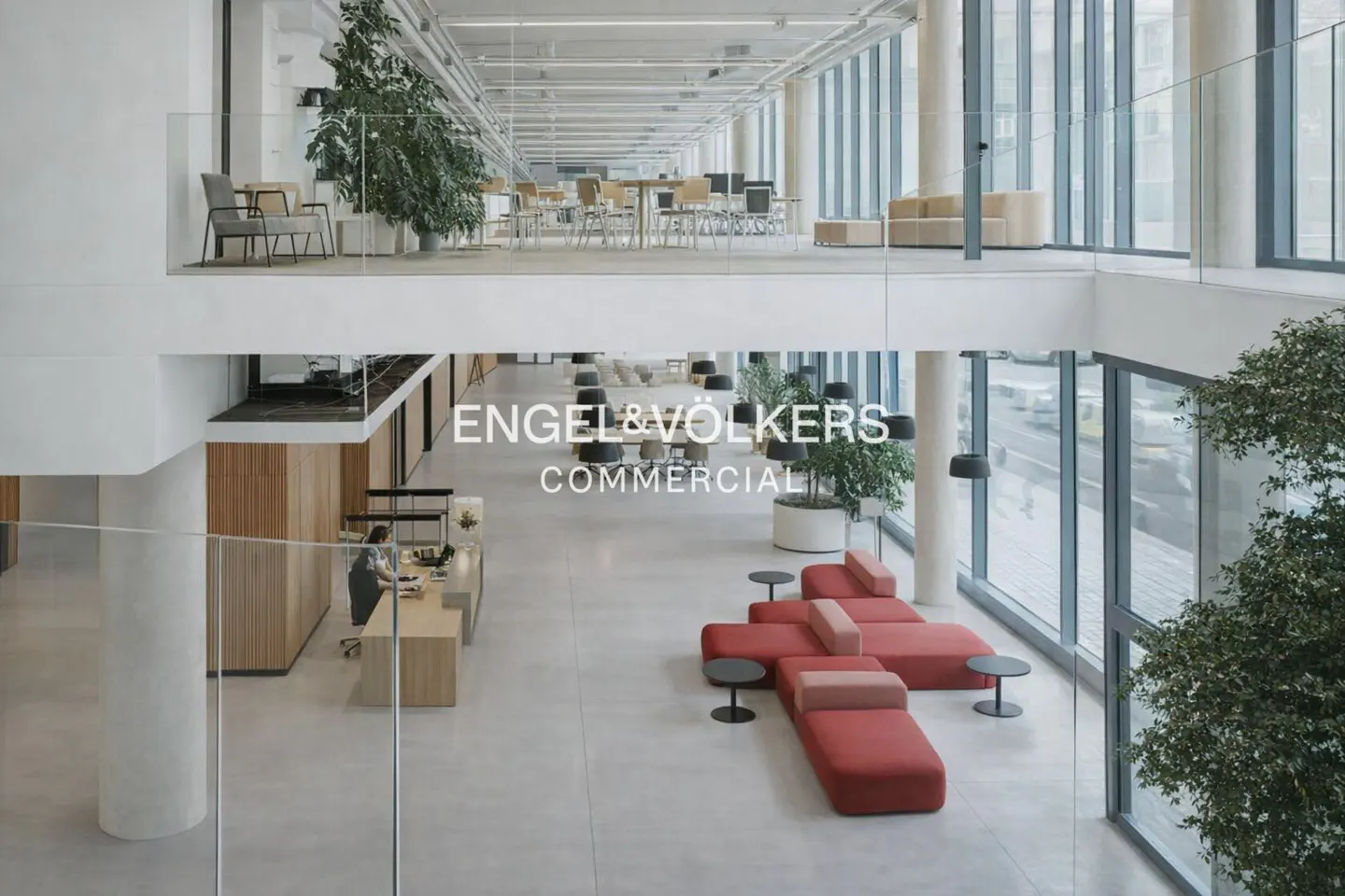 Engel & Völkers Commercial office interior with red modular seating, plants, and a receptionist at a wooden desk.