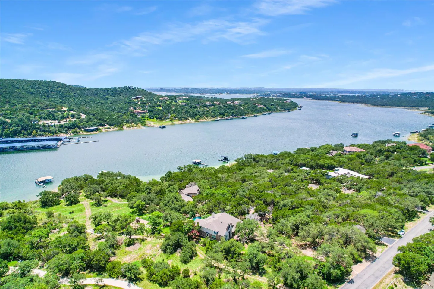 Aerial view of a lake house surrounded by lush green trees under a bright blue sky.