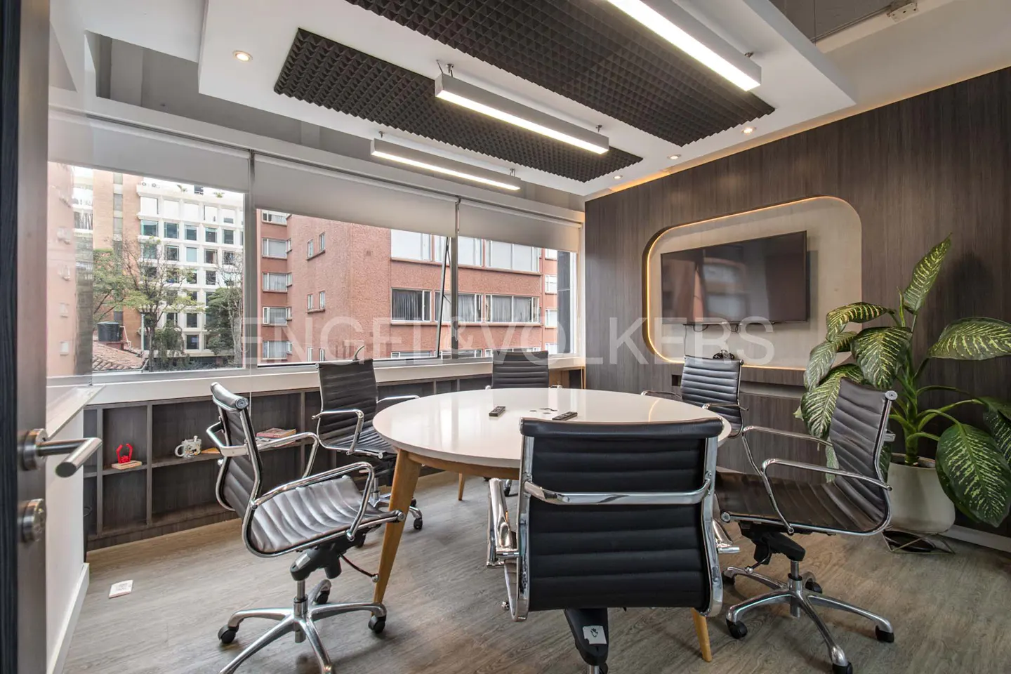 A modern conference room with a round table, black chairs, and a large window with a city view.