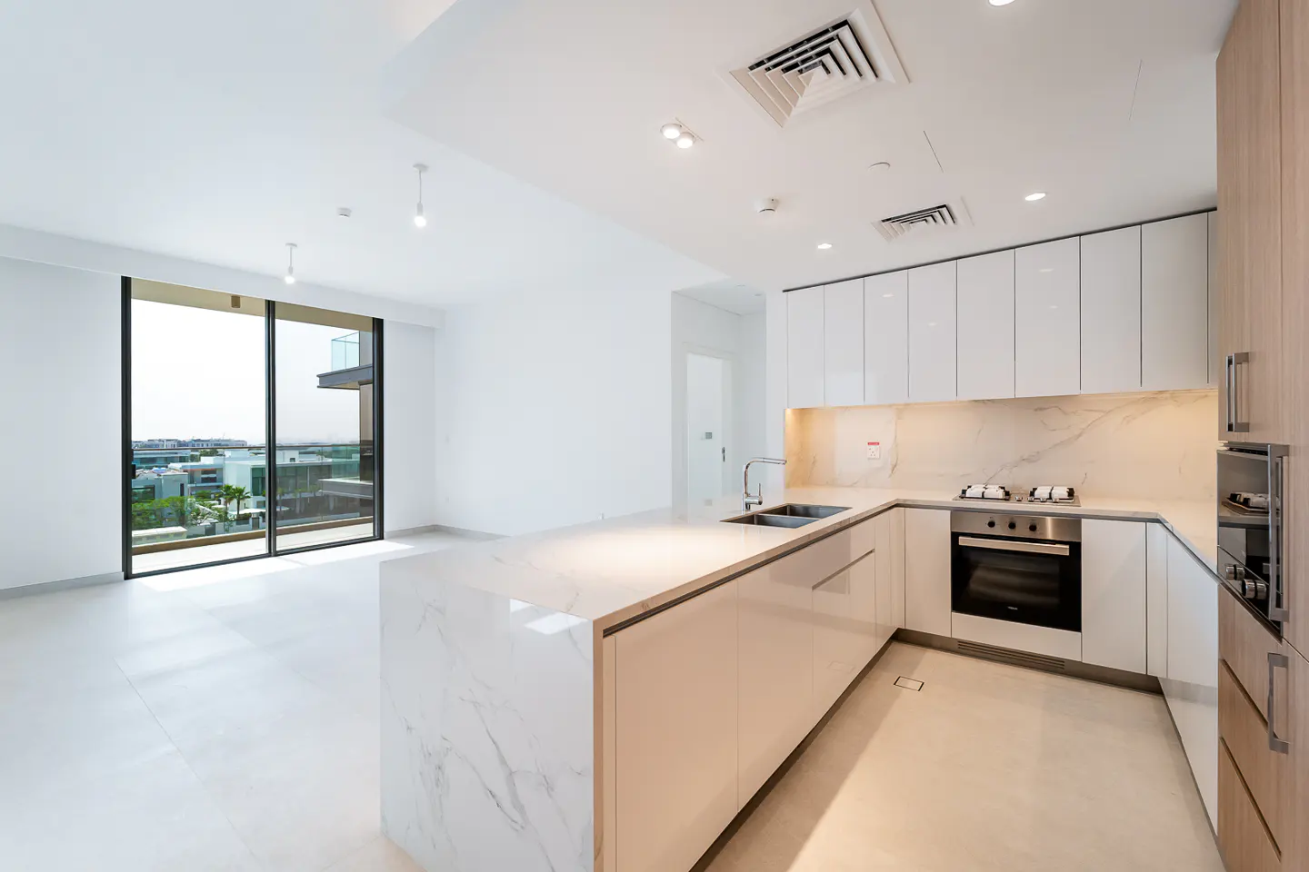 Bright, modern kitchen with white cabinets, marble island, stainless steel appliances, and large windows overlooking a cityscape.