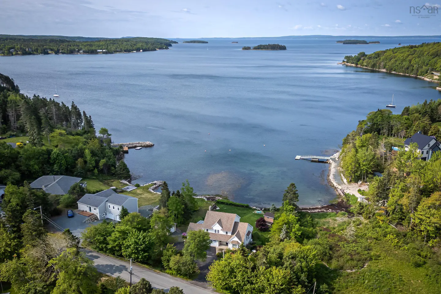 Aerial view of waterfront homes nestled among green trees, overlooking a blue bay with islands and sailboats.