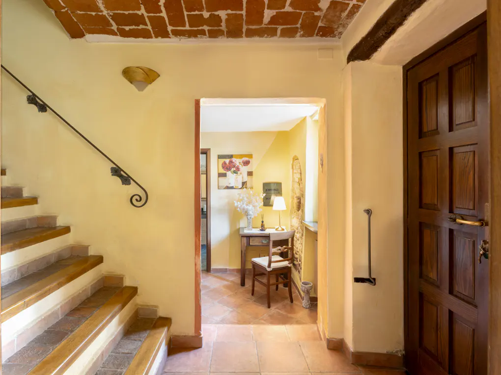 Interior view of a home featuring stairs with a black railing, a doorway to a room with a desk, and a dark wood door.