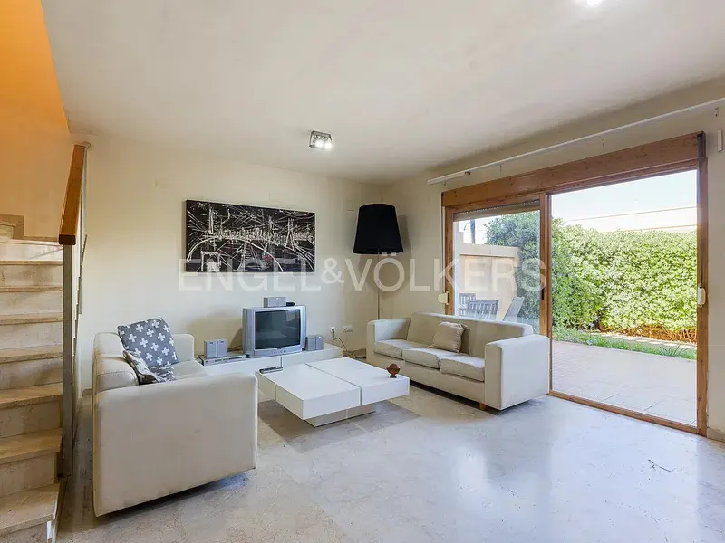 Bright living room with two beige sofas, a white coffee table, a TV, and a large sliding door opening to a garden.