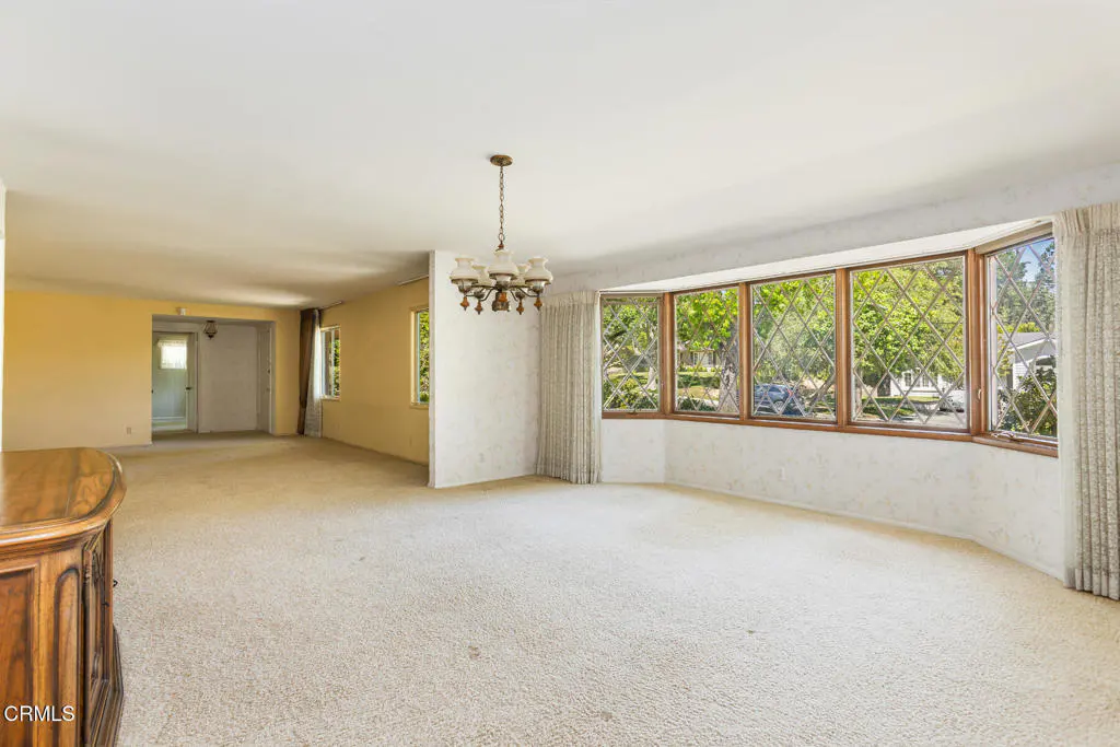 Spacious living room with beige carpet, large bay window with diamond pattern, and vintage chandelier.