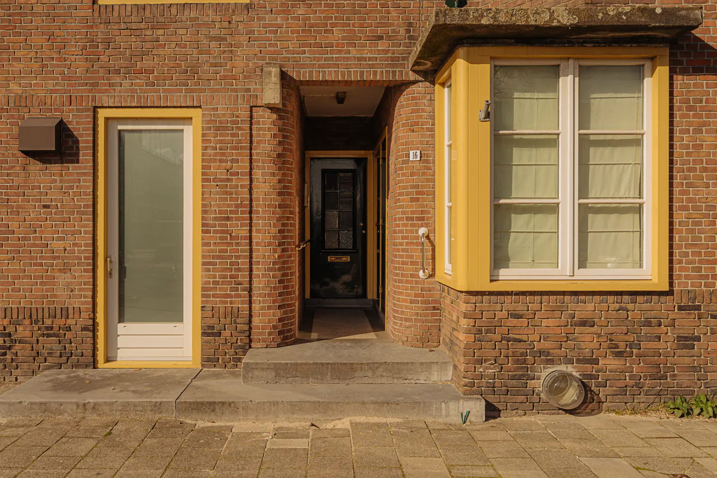 Brick building exterior with a black front door, white side door, and yellow-framed bay window.
