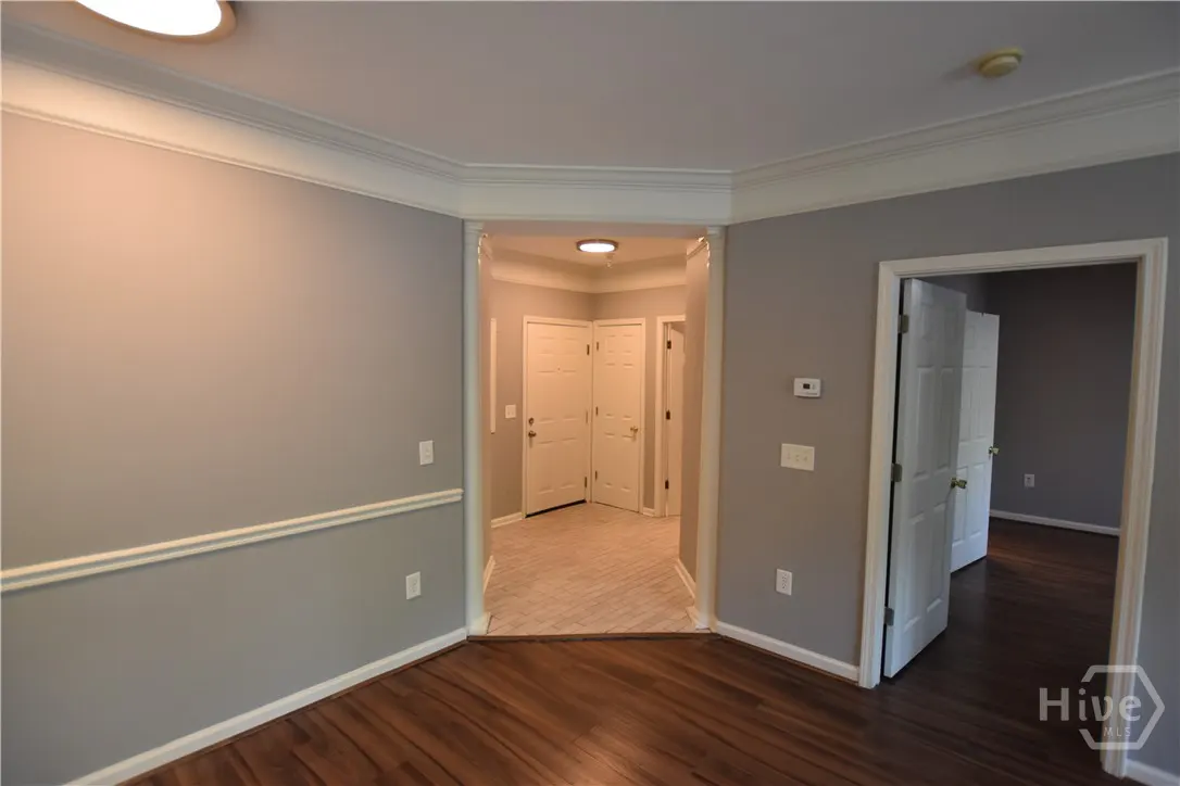 A room with gray walls, white trim, and dark wood floors, looking into a hallway with white doors and beige tile.