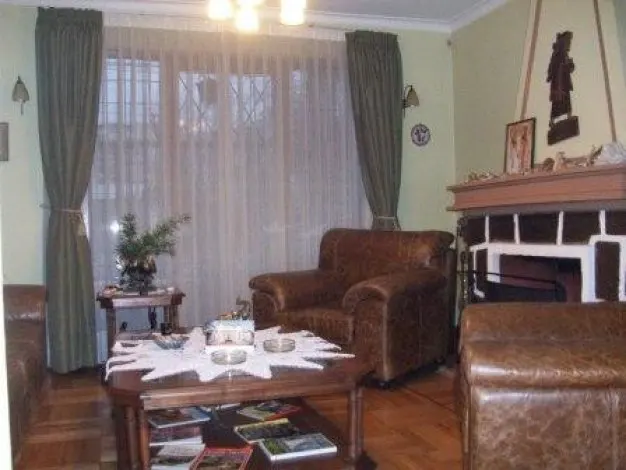 Living room with brown leather armchair, ottoman, and coffee table with magazines. Green curtains frame the window. Fireplace in the background.