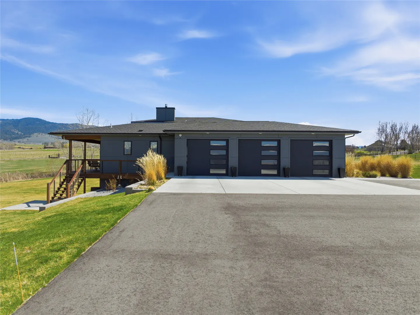 Modern gray house with three-car garage and covered porch. Green lawn and blue sky.