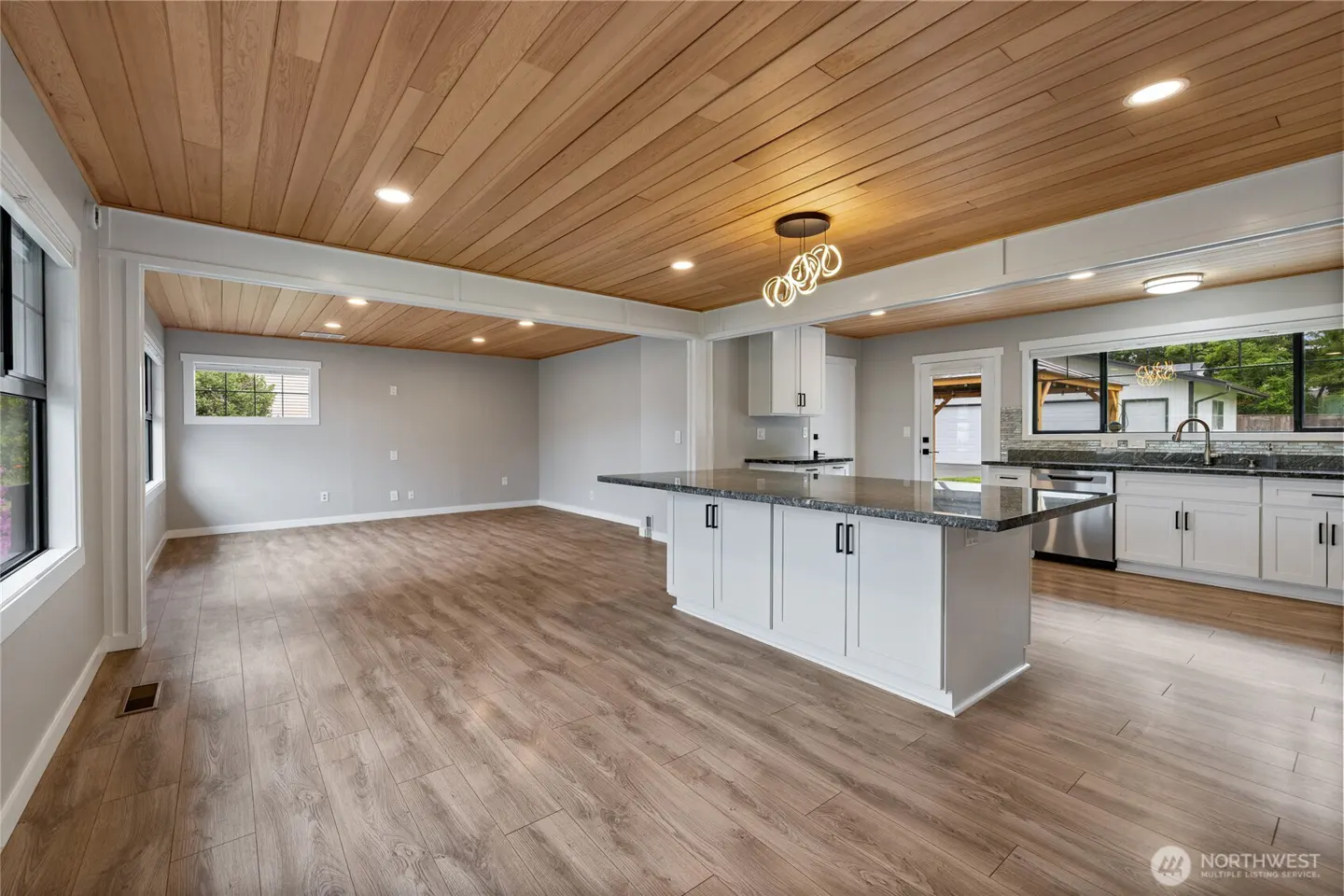 Open-concept kitchen and living room with wood floors and ceiling. White cabinets, gray walls, and a large island.