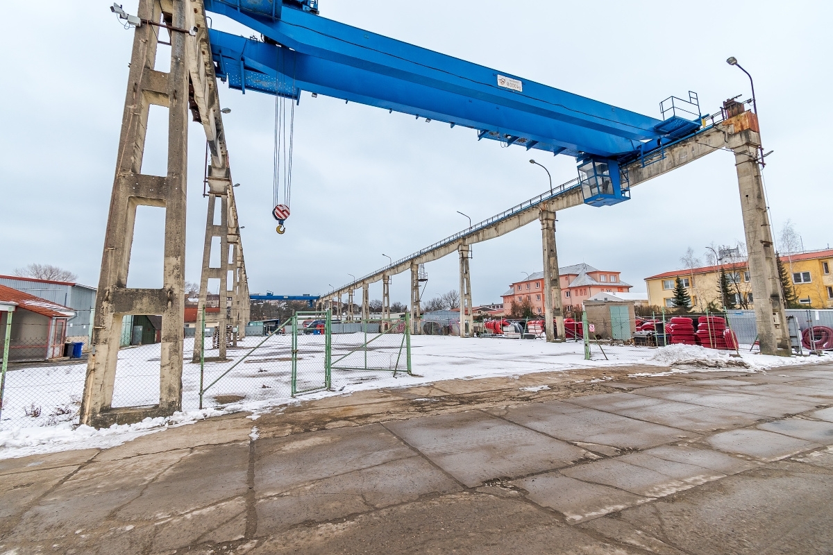 A large blue industrial gantry crane stands over a snowy, fenced-in outdoor storage yard with concrete ground. [AI-generated text]