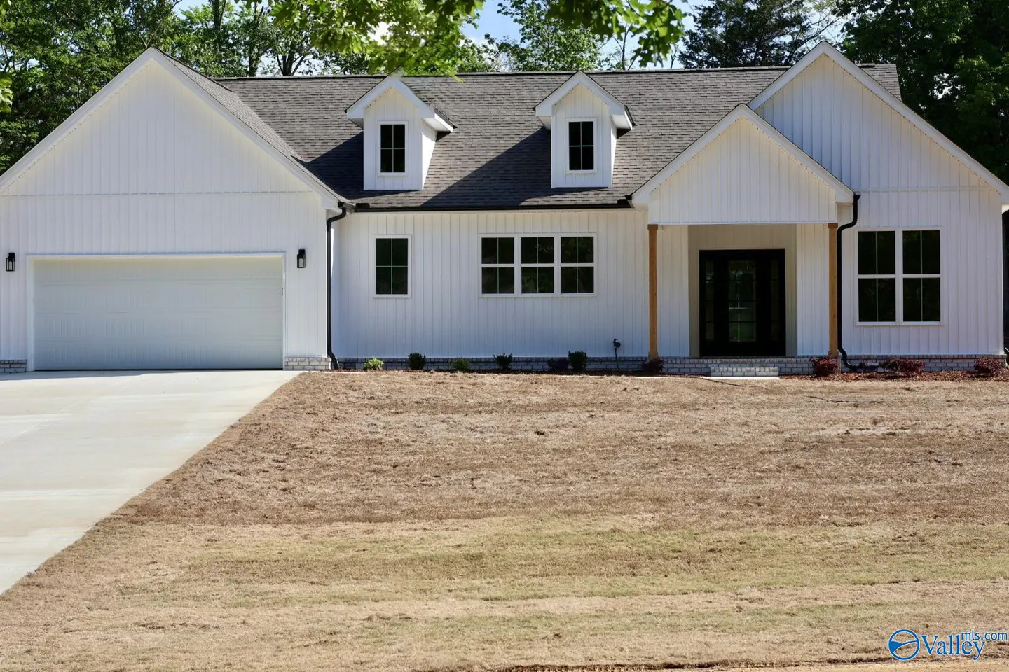 A white, one-story house with a gray roof, black windows, and a two-car garage. The lawn is brown.