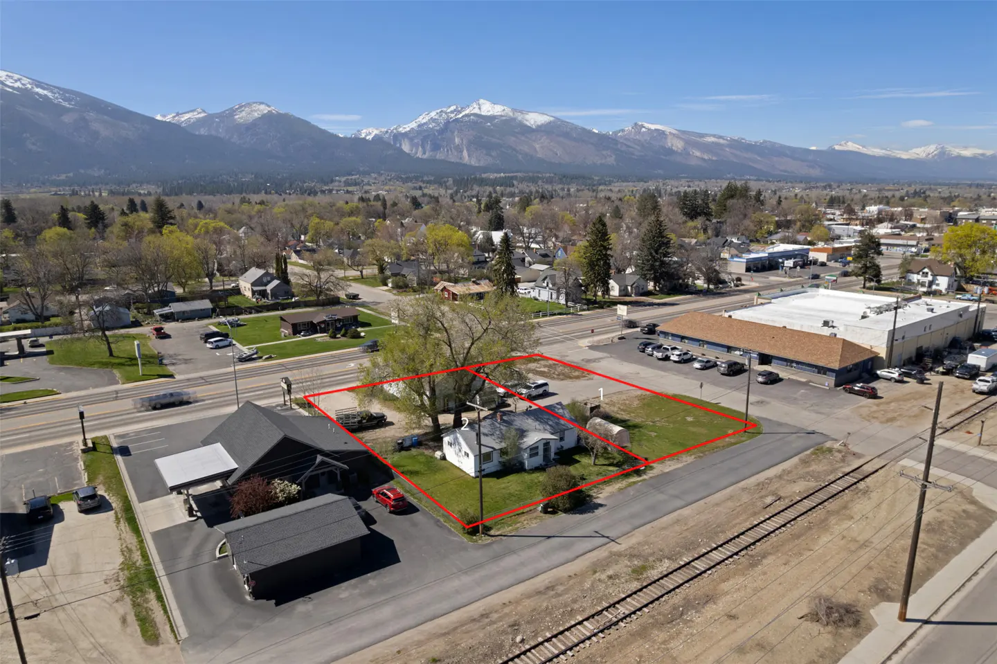 Aerial view of a property outlined in red, with a white house, green lawn, and mountains in the background.