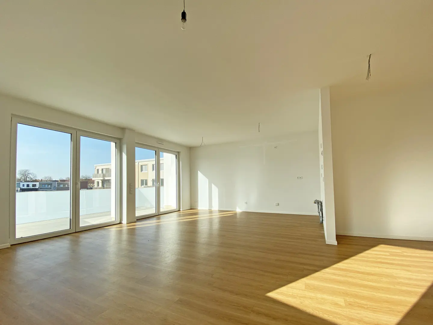 Bright, empty room with wood floors, white walls, and large sliding glass doors to a balcony.