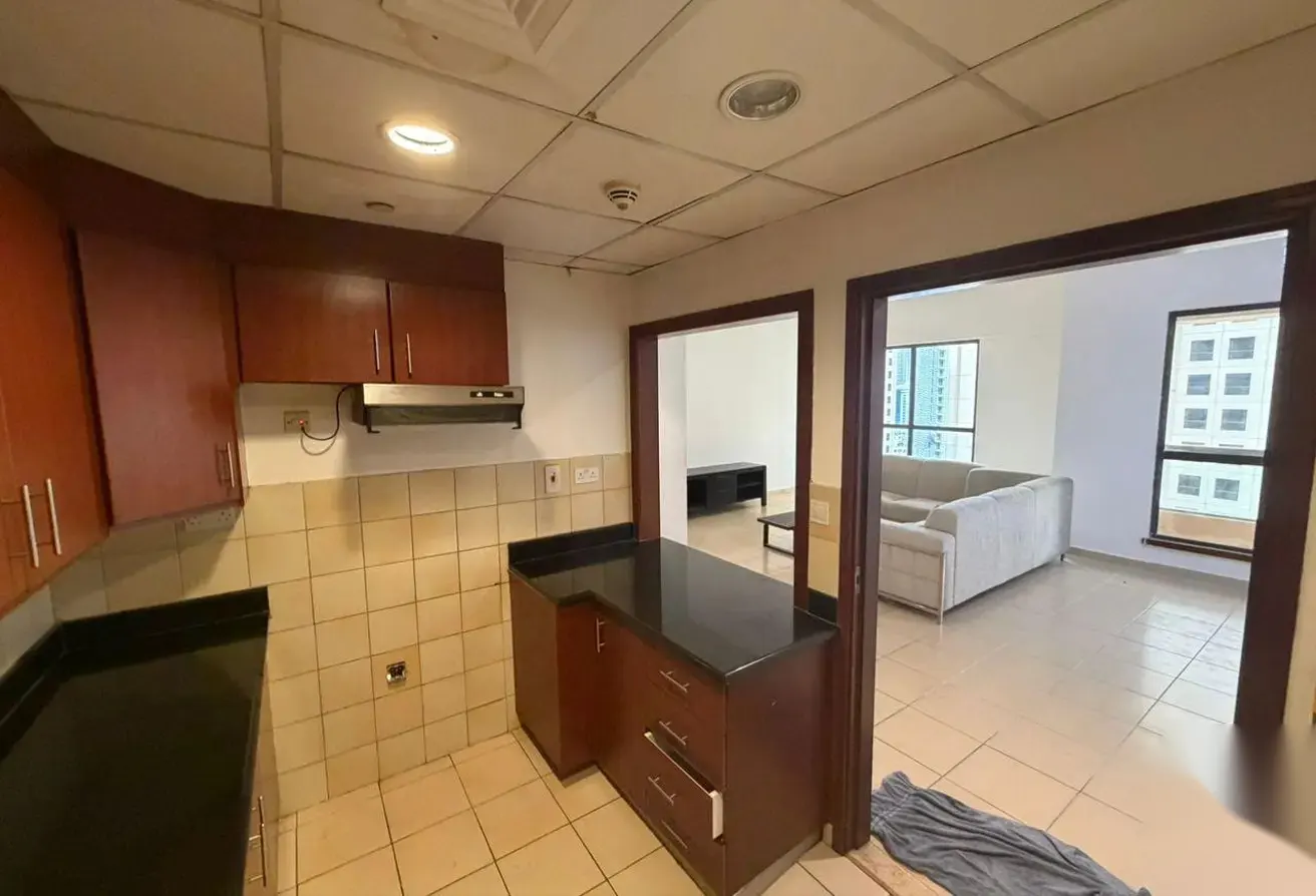 A kitchen with brown cabinets and black countertops, open to a living room with a gray sofa and city view.