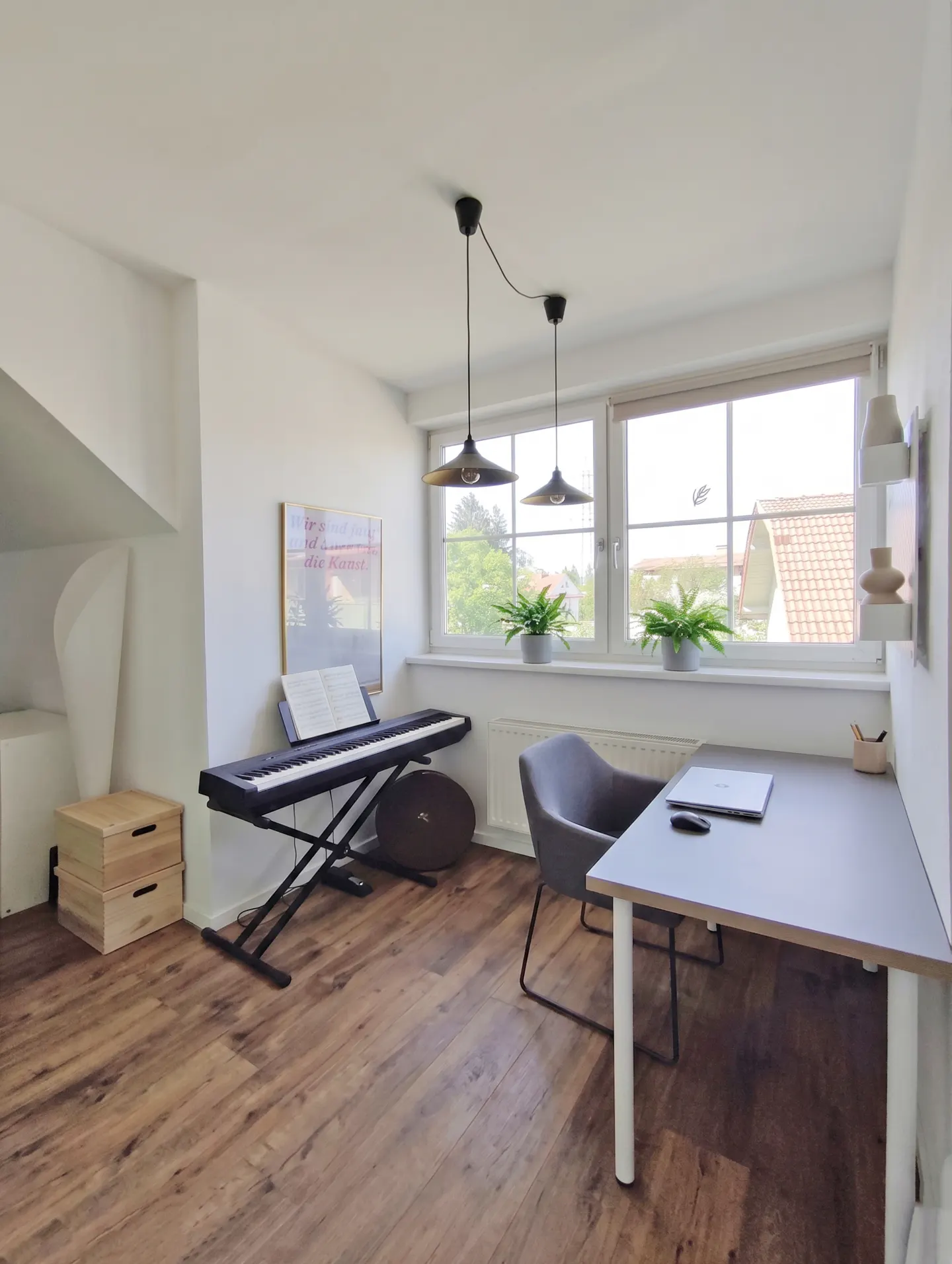 Bright room with wood floors, a desk with a laptop, a gray chair, and a keyboard by the window.