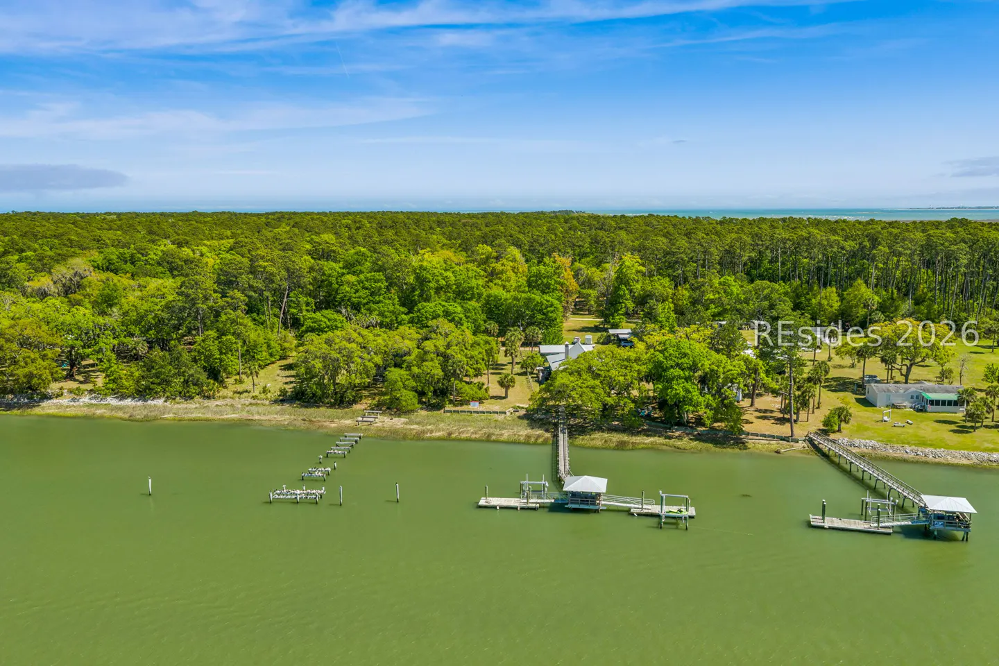 Aerial view of a waterfront property with docks, lush green trees, and a blue sky.