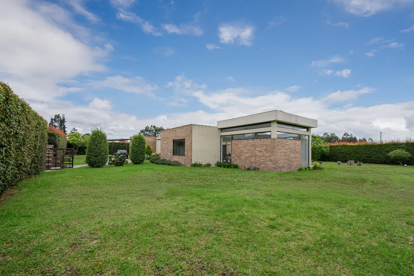 Modern brick home with large lawn, hedges, and blue sky with clouds.
