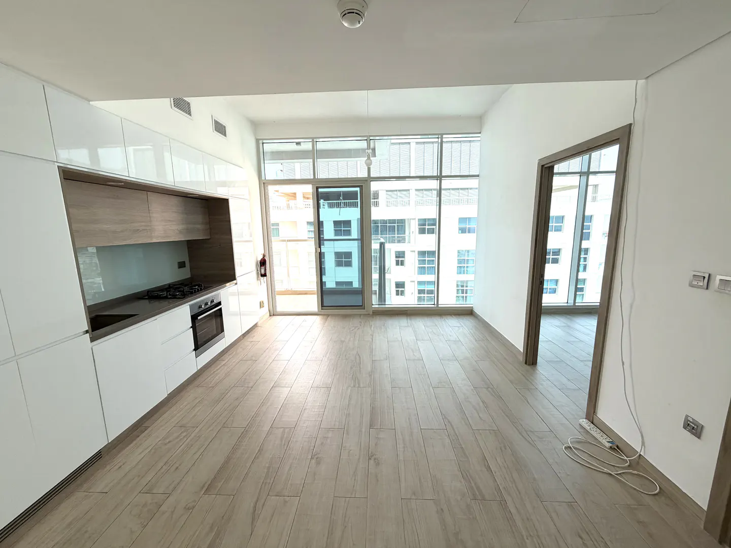 Bright, modern apartment interior with white cabinets, wood floors, and large windows overlooking a city.