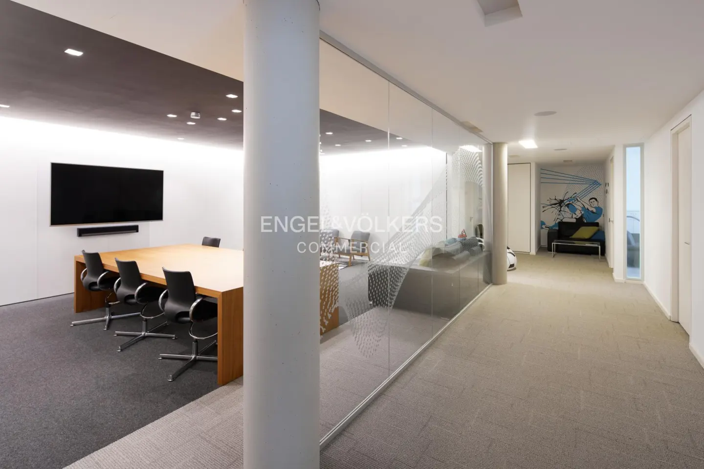Modern office interior with a glass-walled conference room, wooden table, black chairs, and a hallway with wall art.