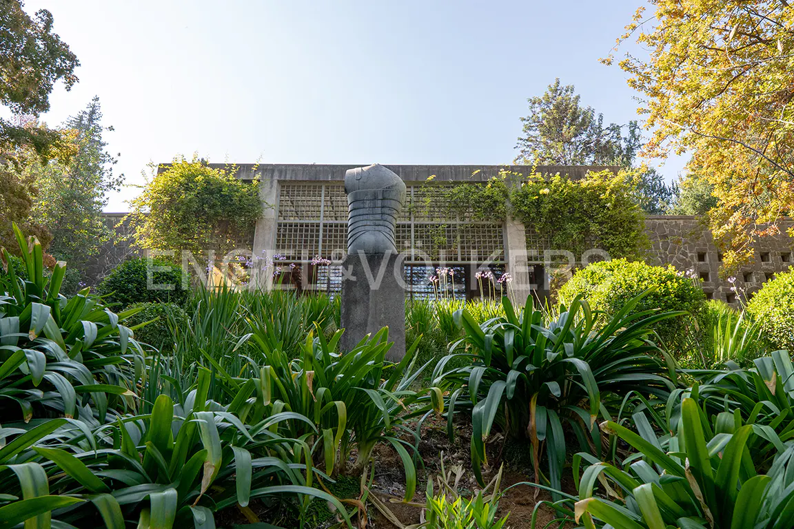 Exterior view of a modern building with a stone sculpture in a lush green garden.