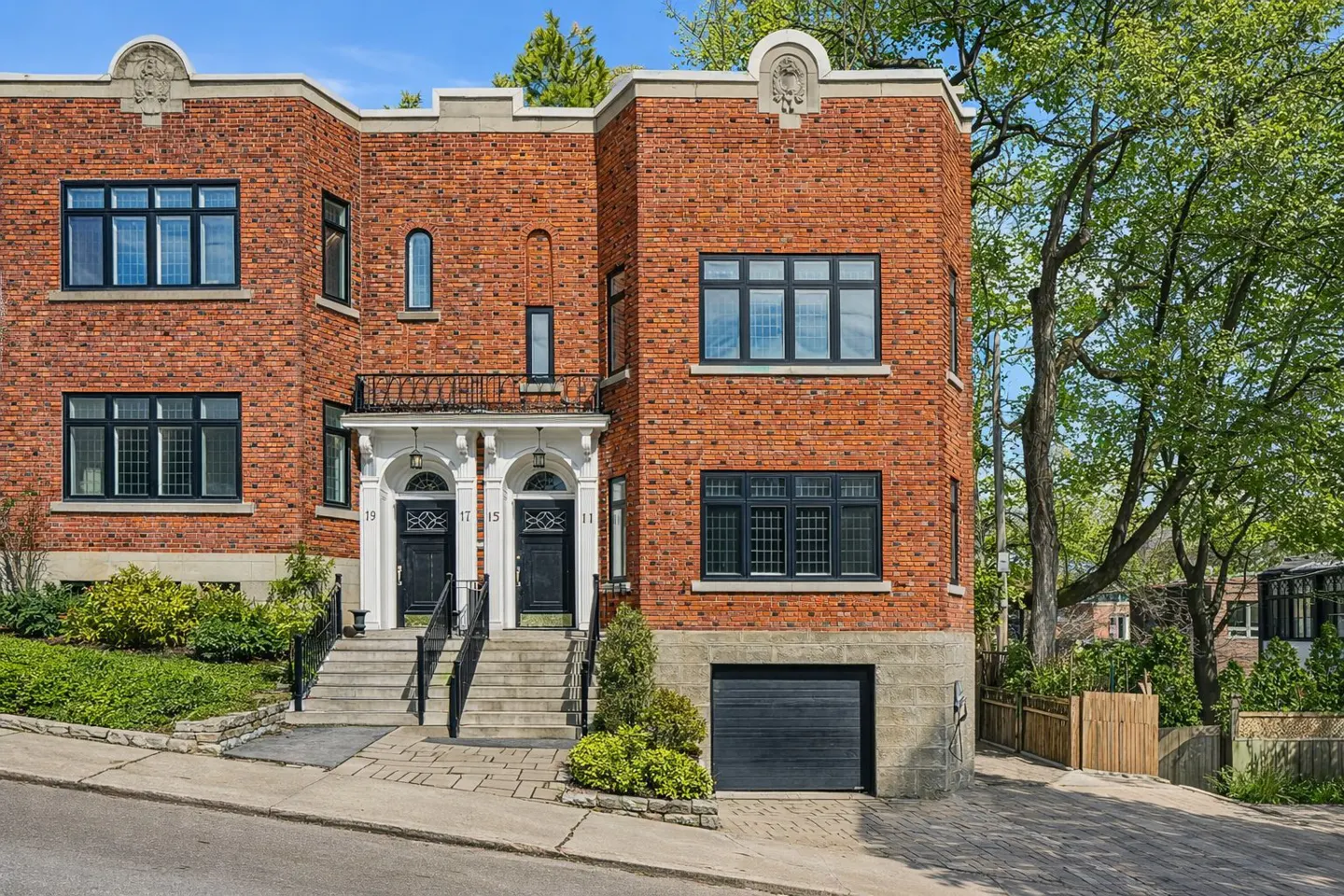 Brick townhouse with black windows, white door frames, and steps leading to black doors. A black garage door is on the right.