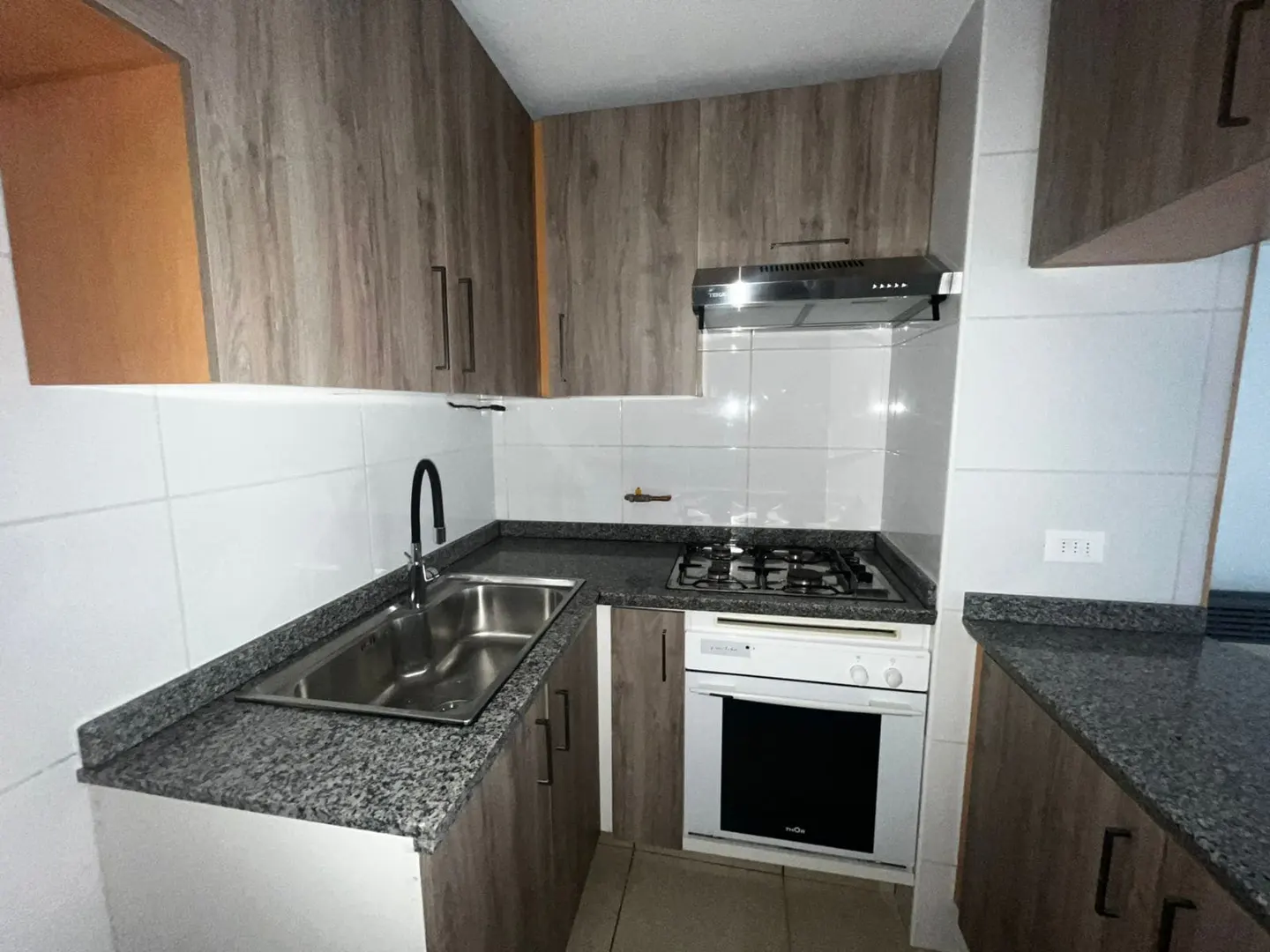 A kitchen with wood cabinets, granite countertops, a stainless steel sink, and a white oven.